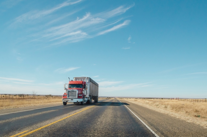 Red Commercial semi truck driving down a rural paved road