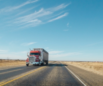 Red Commercial semi truck driving down a rural paved road