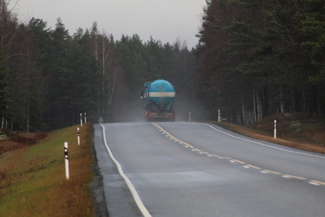 A truck tank vehicle driving down a misty road along many green trees