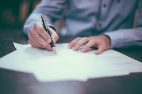 A person signing a piece of paper with a pen.